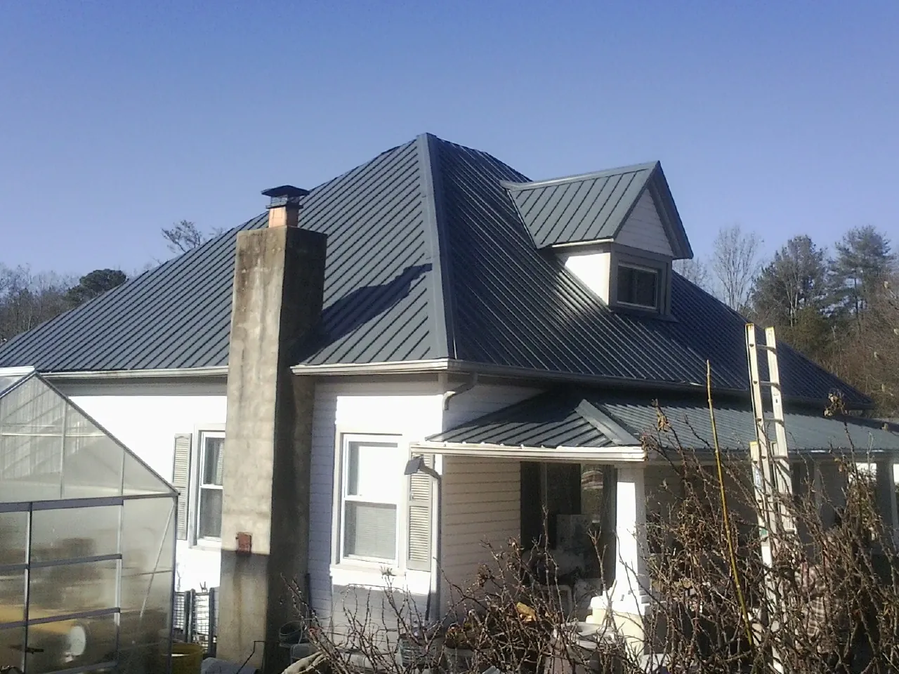Dark blue standing seam metal roof on a white farmhouse with dormer — Slate & Tile Roof Repair by Roofing Brothers in Buncombe