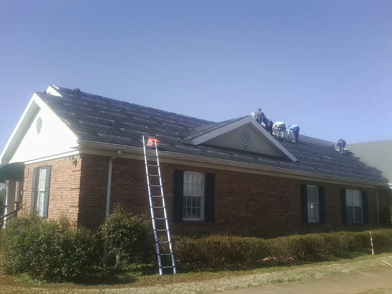 Crew tearing shingles off a brick ranch roof with a ladder set — Metal Roof Repair work by our crew in Buncombe