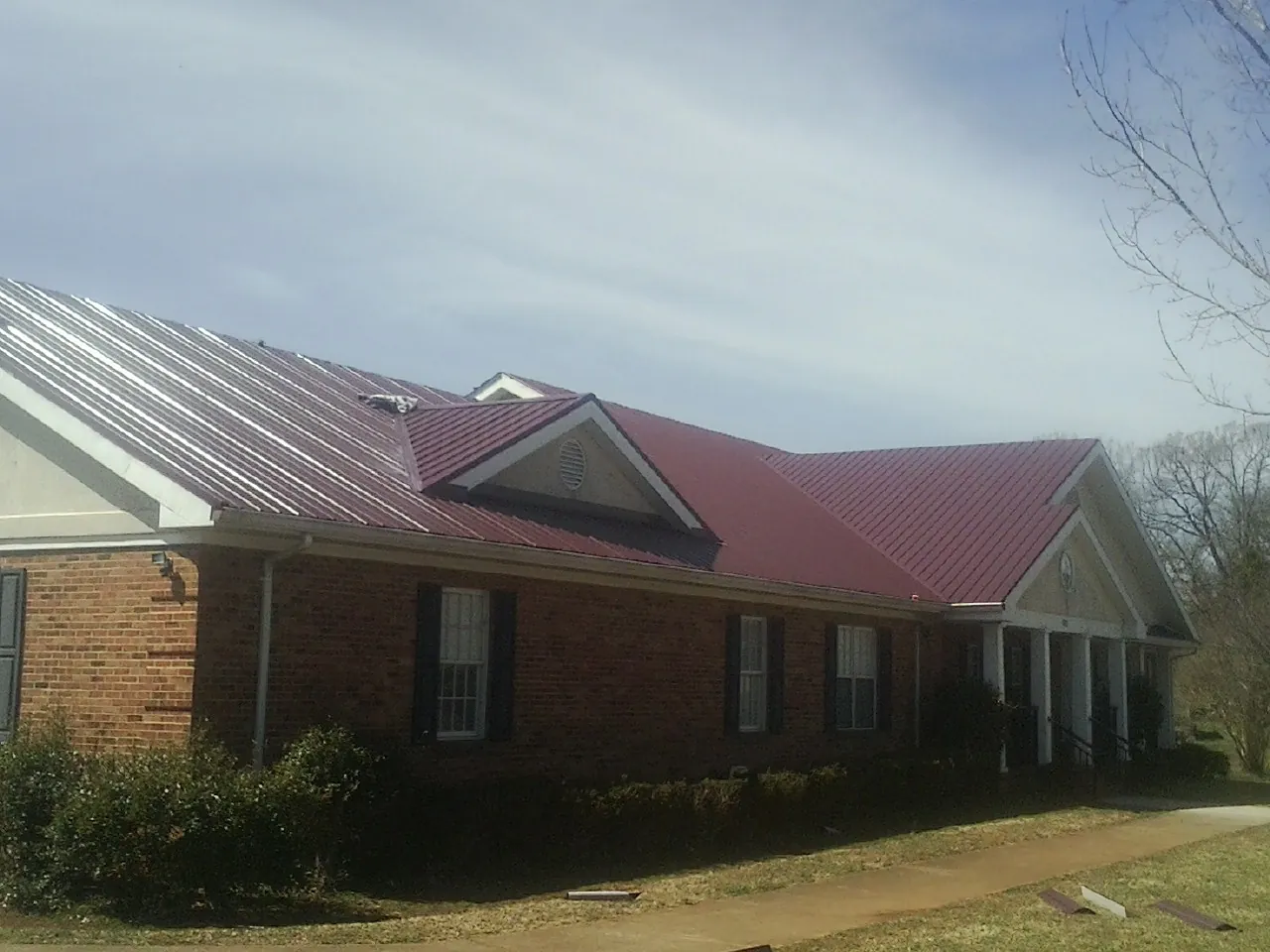 Red metal roof with gabled entries on a long brick building, from a Hail Damage Roof Repair job in Buncombe