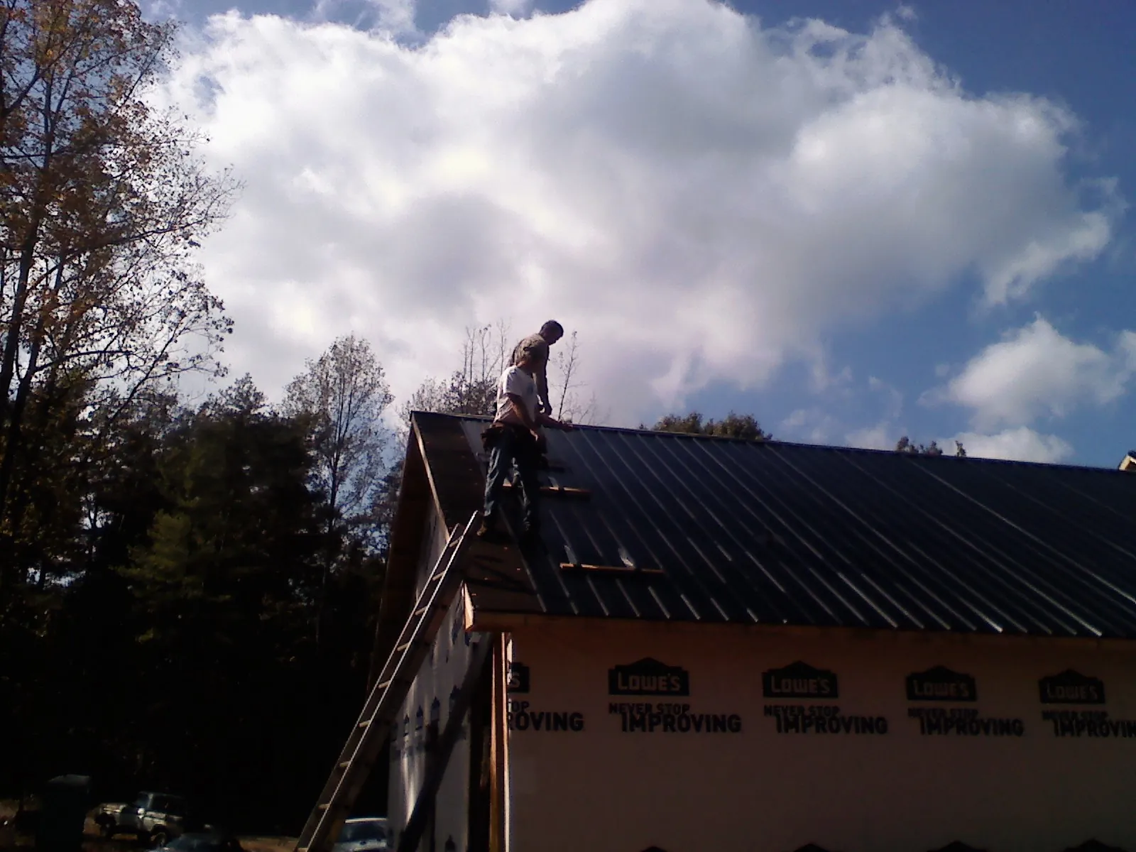 Roofer fastening dark metal panels high against a cloudy sky, from a Roof Inspection job in Buncombe