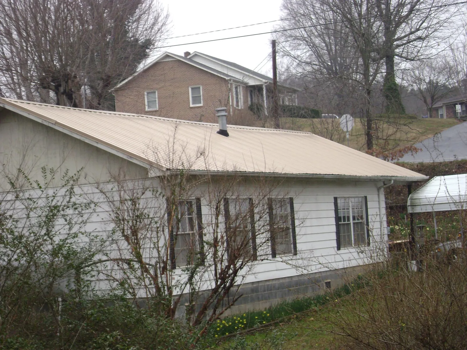 Tan metal roof on a white sided house set into a hillside — Commercial Roofing by Roofing Brothers in Buncombe